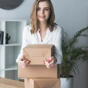 portrait of smiling self-employed businesswoman with parcels looking at camera at home office