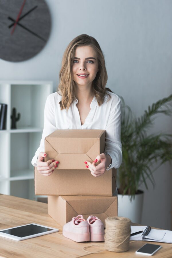 portrait of smiling self-employed businesswoman with parcels looking at camera at home office