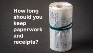 A thick roll of till receipts, held together with an elastic band. Overlaid text reads "How long should you keep paperwork and receipts?"